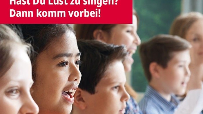 Kinder, die in einem Chor singen, einige halten Notenblätter, mit einem deutschen Text über ihnen.