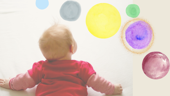 Ein Baby liegt auf dem Bauch und schaut an die Wand mit bunten Farbklecksen.