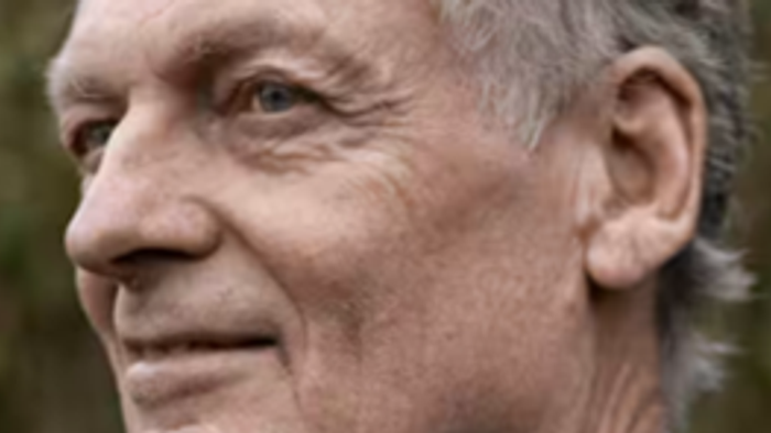 Gråhåret mand iført jakkesætjakke over en blå skjorte.