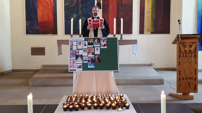 Ein Mann in einer Kirche hält ein Buch, umgeben von Kerzen und gerahmten Fotos.
