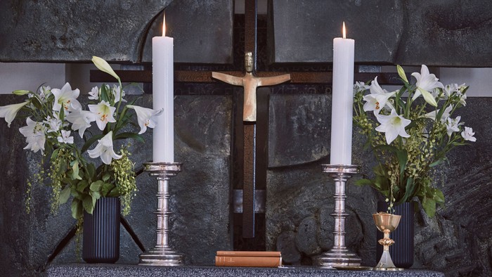 En altertavle med kors, to lysestage med lys, to blomsterarrangementer og en bibel