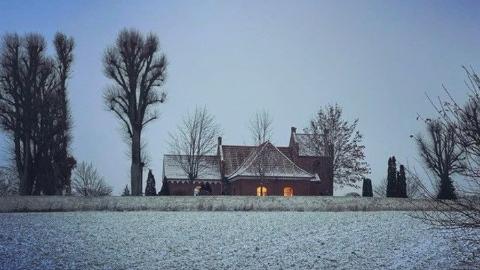 En snedækket gård med et stort hus og nøglerne træer i en vinterlandskab