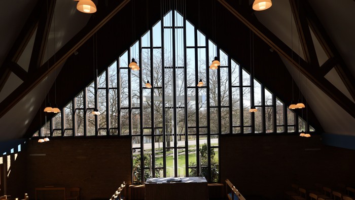 Moderne kapelinteriør med høje farvede glasvinduer og varme hængende lamper, der oplyser træbænkene.