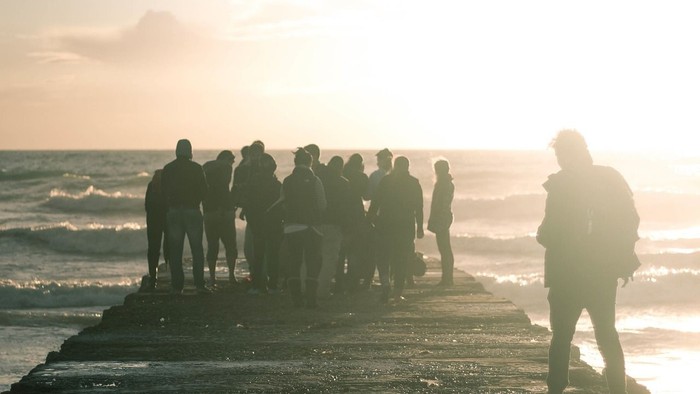 Eine Gruppe von Menschen steht am Strand bei Sonnenuntergang.