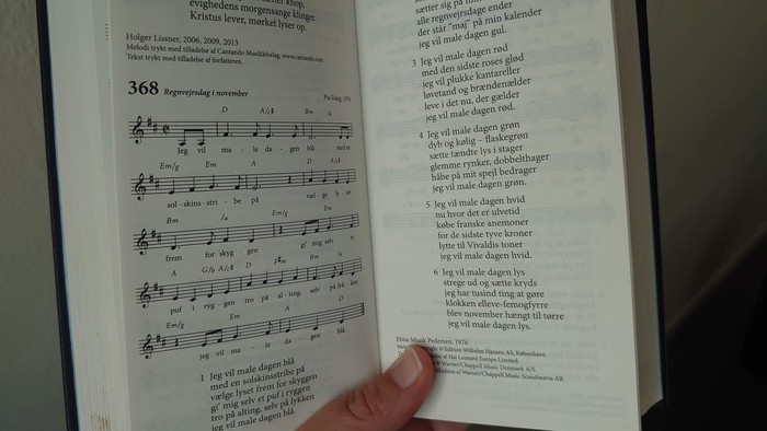 Hånd holder åben bog med noter og tekst på dansk