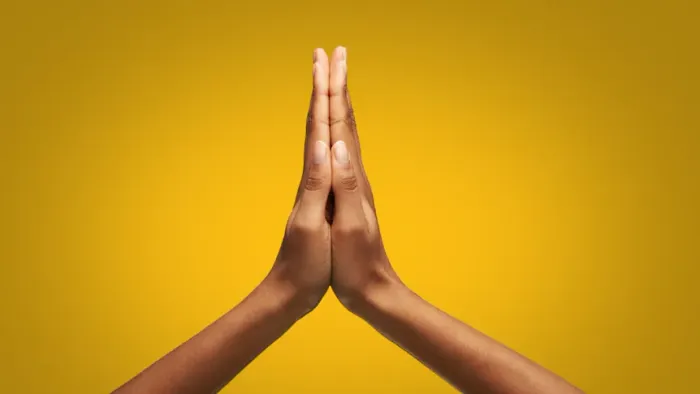 Hands pressed together in front of yellow background.
