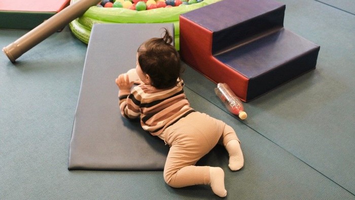 Ein Baby im Strampler spielt mit einem Ball in einer bunten Spielecke.