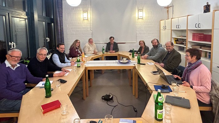 Eine Gruppe von Menschen sitzt an einem Tisch in einem modernen Raum und diskutiert.