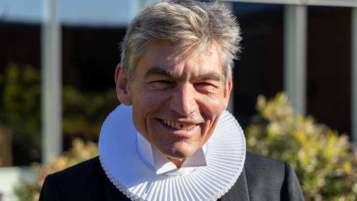 Mand med kruset krave smiler.