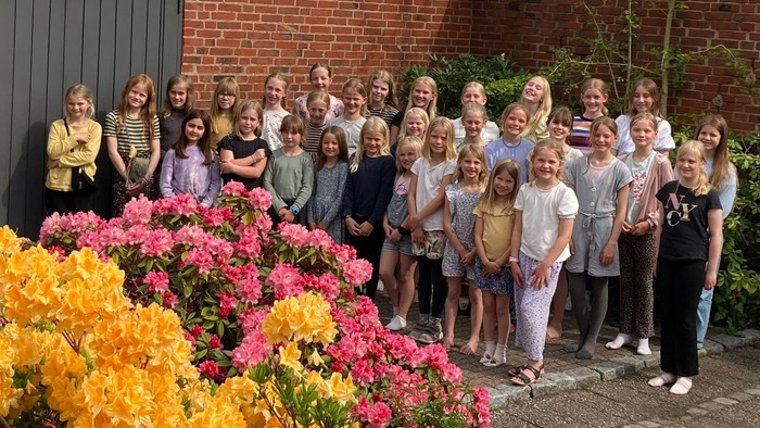 En gruppe børn står foran en mur med blomster.