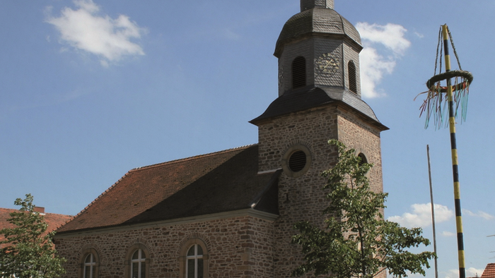 Kirchengebäude mit Turm und Wetterfahne unter blauem Himmel