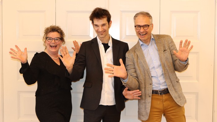 Tre mennesker står sammen med åbne arme og smilende ansigter.