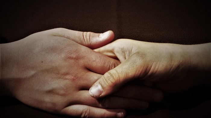 Zwei Hände, die sich halten, mit verschränkten Fingern.