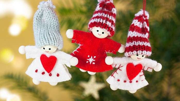 Drei gestrickte Weihnachtsbaumanhänger hängen an einem Baum, jeder mit einem Herz und einer gestreiften Mütze.