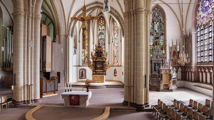 Großzügige Kircheninneraum mit hohen Bögen, bunten Glasfenstern und einem Altar im Mittelpunkt