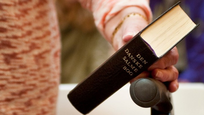 En person holder en dansk bibel på et mikrofonstativ under det, der ser ud til at være en oplæsning eller gudstjeneste.