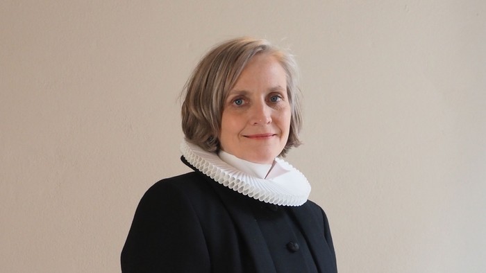 Kvinde i sort kaptajnmø, hvid krage og hvid kuffe.