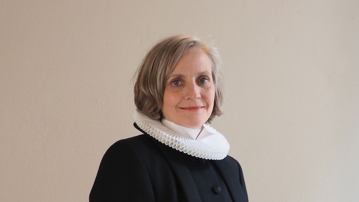 Kvinde i sort kaptajnmø, hvid krage og hvid kuffe.