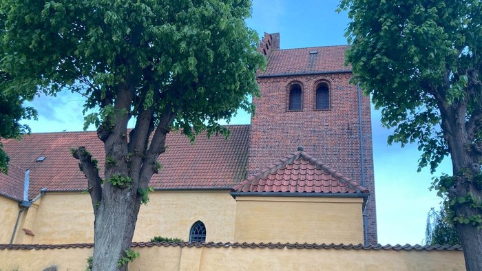 Et gult kirkebygning med røde tag og en klokketårn mellem træer