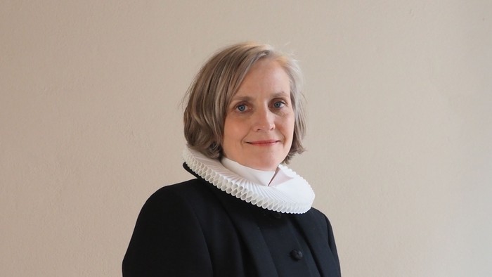 Kvinde i sort kaptajnmø, hvid krage og hvid kuffe.