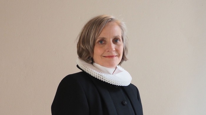 Kvinde i sort kaptajnmø, hvid krage og hvid kuffe.