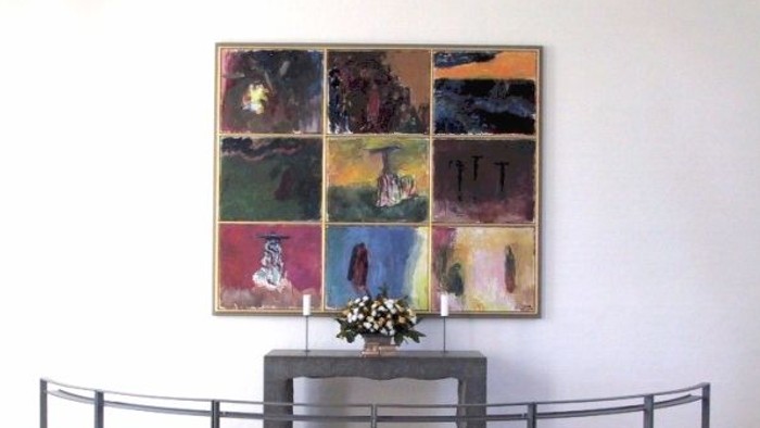 En stor maleriudstilling på væggen med en lille bord med blomster i forgrunden og en kurvet bænke foran