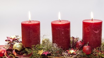 Tre røde lysstaker med lys på, omgivet af grønne planter og røde og grønne pynt.