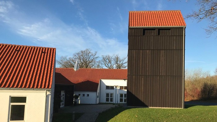 En moderne bygning med rød tag og en høj, træklædt tårn ved siden af en hvid bygning med rød tag og græsplæne foran