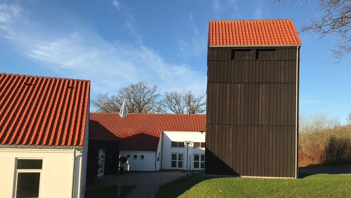 En moderne bygning med rød tag og en høj, træklædt tårn ved siden af en hvid bygning med rød tag og græsplæne foran