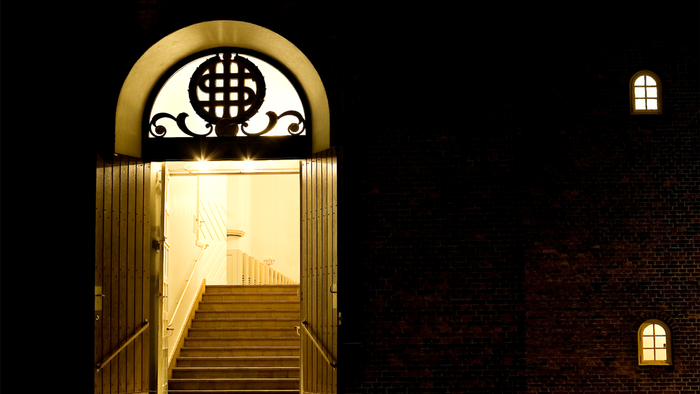 En belyst indgang til et stort hus med trappe opad og to vinduer på væggen.