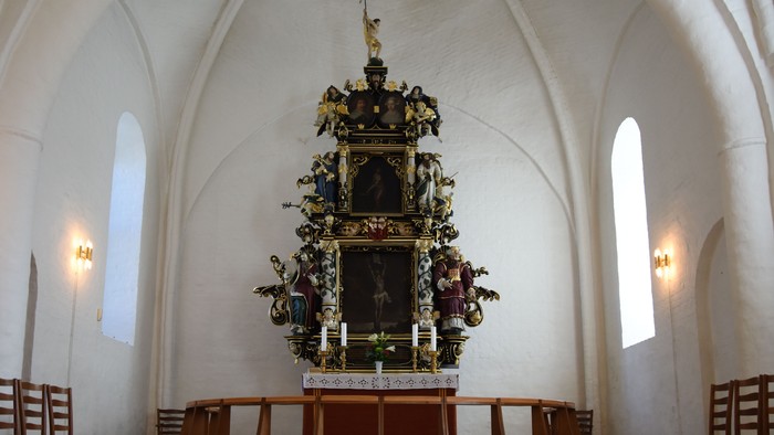 Indre del af kirke med altertavle og bænke.