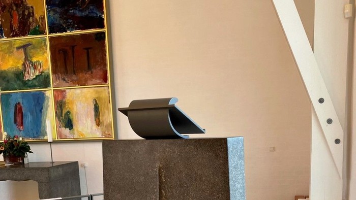 En stor sten med et udhugget kors står i et rum med billeder og trappe.