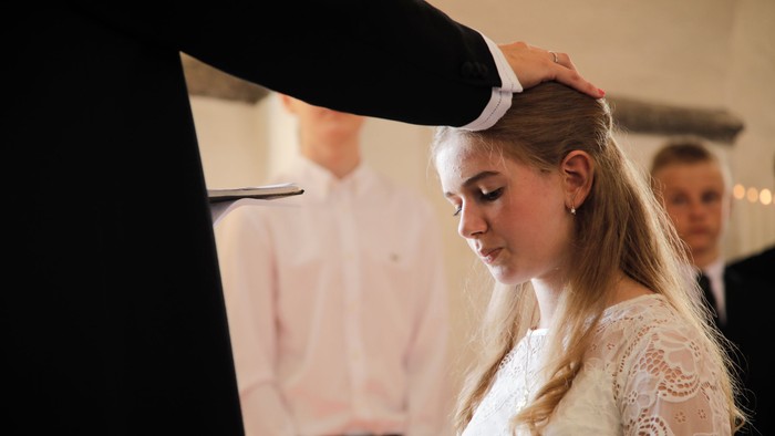 En kvinde i en hvid kniplingskjole får justeret sit hår af en mand under en formel ceremoni.