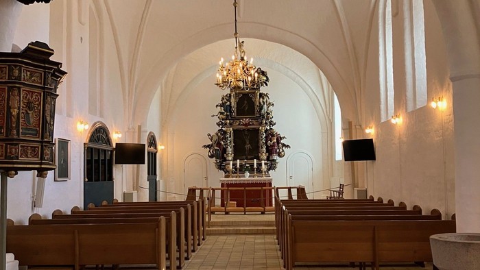 Elegant kirkeinteriør med træbænke, hvælvede lofter og et prægtigt alter belyst under blødt lys.