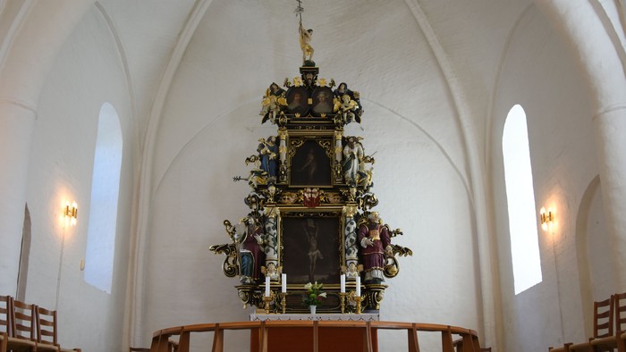 Alter i kirke med udsmykket altartavle og lys.