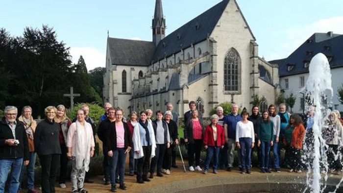 Eine Gruppe von Menschen steht vor einer Kirche mit einem Brunnen.