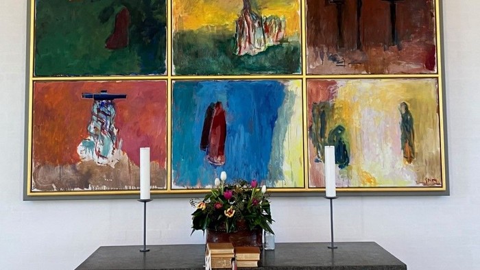 En række farvede malerier på veggen over en bord med blomster og lysstake