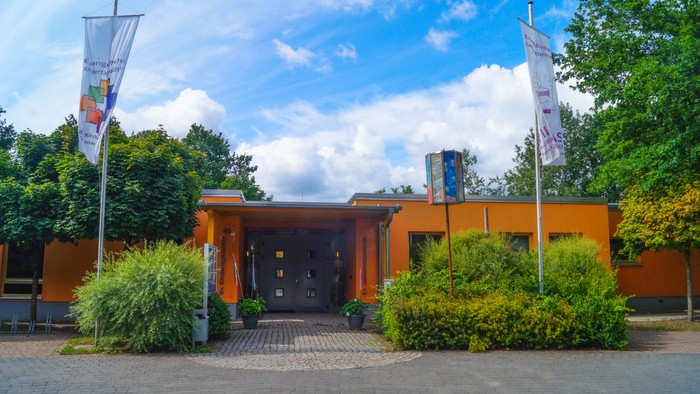 Ein modernes Gebäude mit zwei Fahnen und Grünpflanzen vor dem Eingang