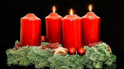 Fire tændte røde stearinlys omgivet af grønne planter og julepynt.