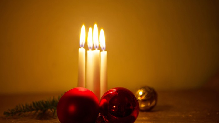 En lyse julelygte med tre lysende lys og tre røde og guld farvede glitrende kugler på en bord.