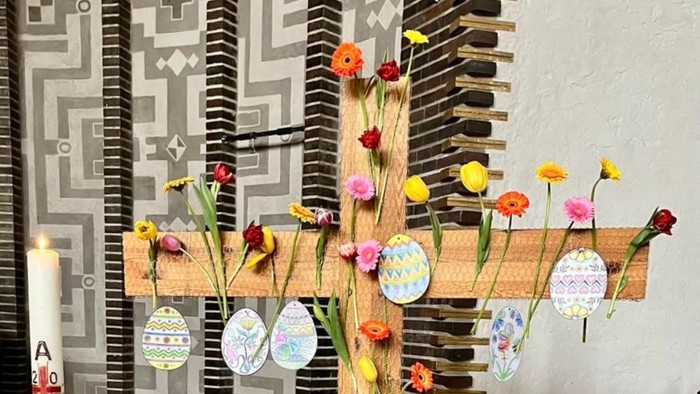 Holzkreuz mit Blumen und Papierostereiern geschmückt