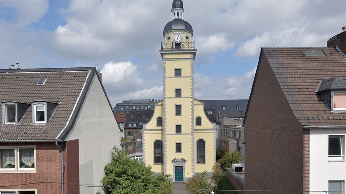 Eine charmante Stadtansicht mit einem hohen Uhrturm, gesäumt von malerischen Gebäuden und einem Schild für ein Freiluft-Orgelkonzert.