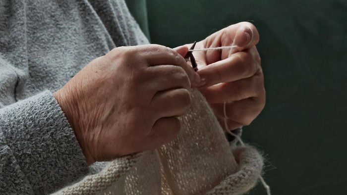 Hände, die mit weißer Wolle stricken.