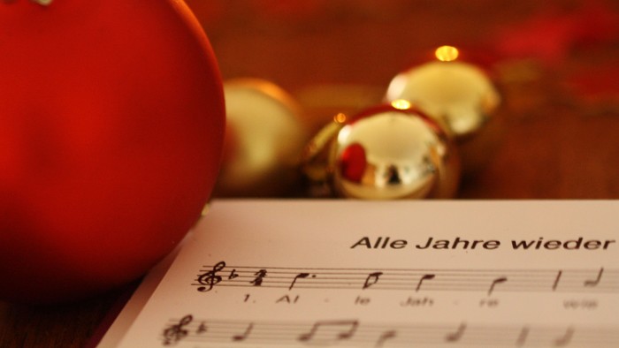 Ein roter Christbaumschmuck mit Uhr und goldene Kugeln auf Notenblatt