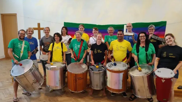 Gruppe von Personen, die mit Trommeln posieren, einige tragen grüne und gelbe Shirts.