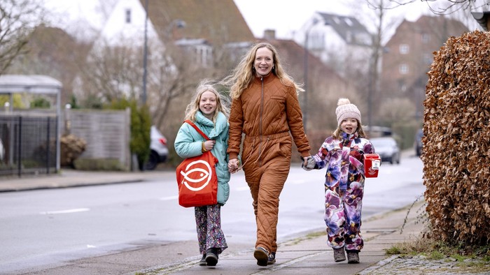 En kvinde går med to børn på en vej i et boligområde