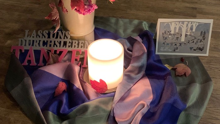 Elegante Einrichtung mit Kerze, Blumenarrangement, buntem Schal und einem Vintage-Foto auf einer gemütlichen Matte.