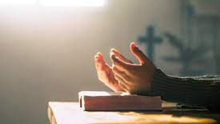 Hands clasped in prayer over an open book on a table.