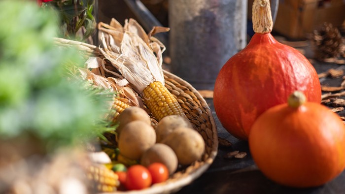 Eine rustikale Erntedekoration mit Kürbissen, Mais, Tomaten und getrockneten Kräutern in geflochtenen Körben.