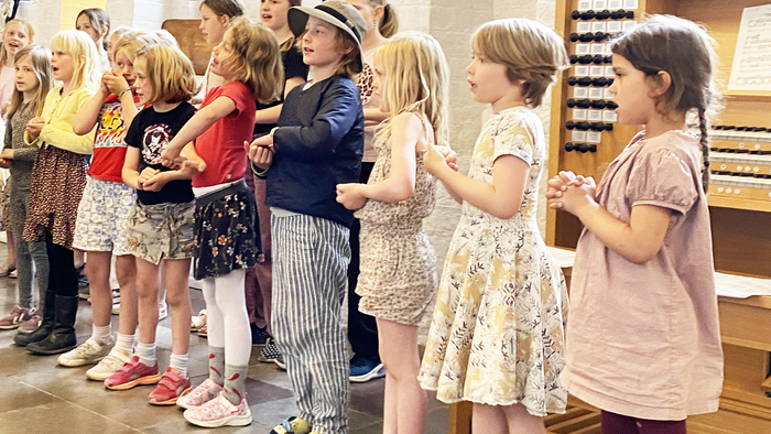 Børn og voksne deltager i aktivitet i kirkehal.